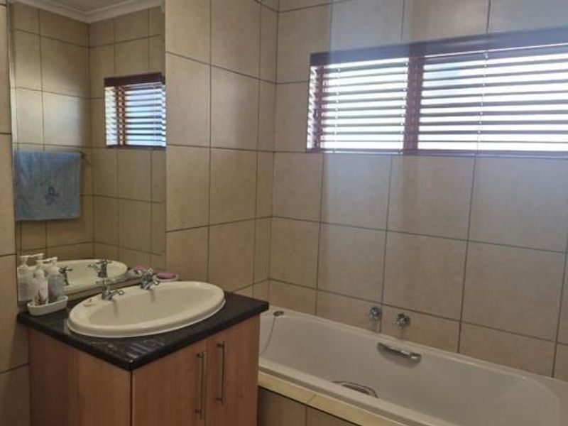 A functional bathroom featuring a built-in vanity with an inset basin, a bathtub, and neutral wall tiling throughout.