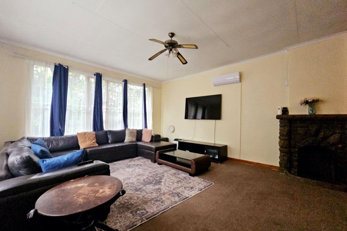 A spacious living room featuring a stone fireplace, ceiling fan, and wall-mounted air conditioning unit, with large windows providing natural light.