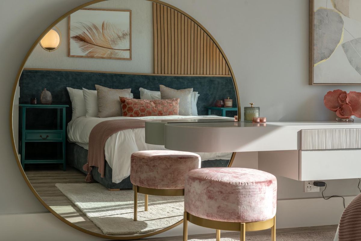A modern, well-appointed bedroom featuring a large circular wall mirror, decorative timber slat wall paneling, and a plush upholstered headboard.