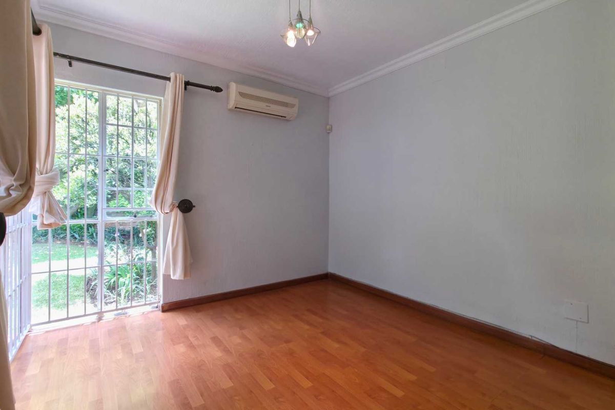 A bright, empty bedroom featuring laminate wood flooring, a wall-mounted air conditioning unit, and a glass sliding door providing access to the garden.