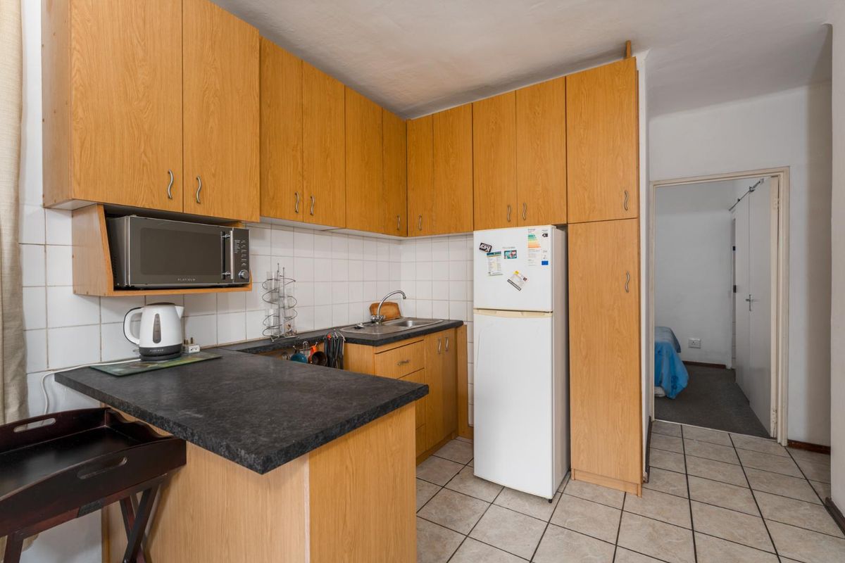 Compact kitchen featuring light wood-tone cabinetry, dark laminate countertops, tiled backsplash, and tiled flooring, offering functional storage and preparation space.