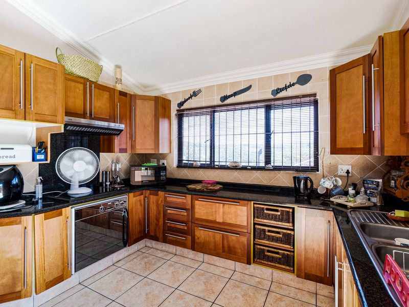 A functional kitchen featuring warm-toned wooden cabinetry, dark granite countertops, a built-in oven with extractor fan, and practical tiled flooring and backsplash.