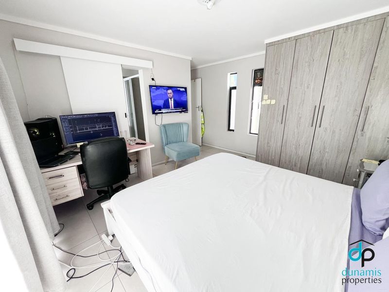 A functional bedroom featuring neutral tiled flooring, built-in wooden cupboards, and a sliding door providing access to the rest of the home.