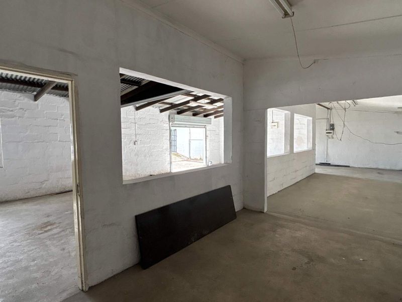 An open-plan industrial utility space featuring exposed roof trusses, concrete flooring, and painted masonry walls, suitable for workshop or storage use.