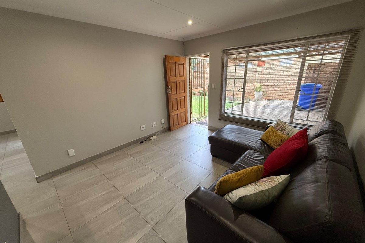 A bright living room featuring large format floor tiles, recessed ceiling lighting, and direct access to an outdoor patio area through a wooden door.