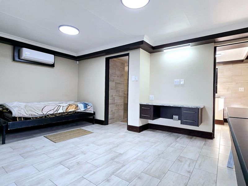 A well-maintained bedroom featuring tiled flooring, a built-in desk, split-system air conditioning, and direct access to an en-suite bathroom.