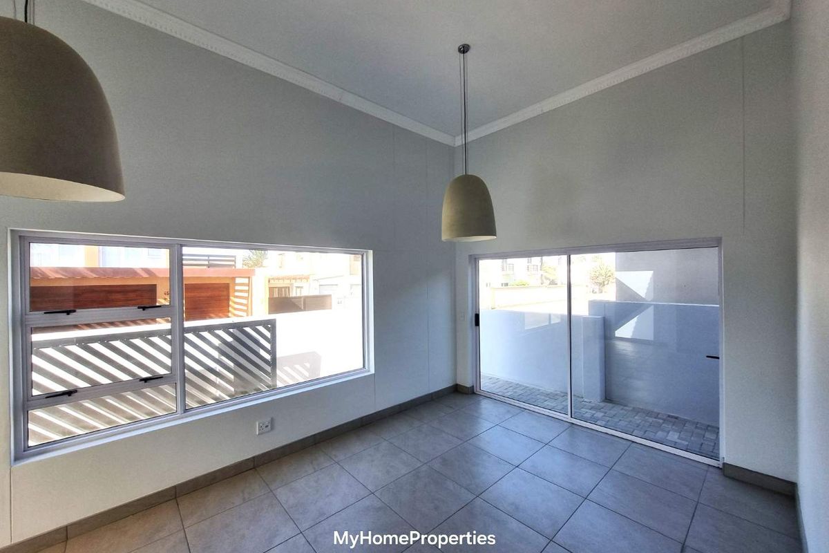 A bright, empty living area featuring large windows, sliding glass doors leading to an outdoor space, tiled flooring, and modern pendant lighting.