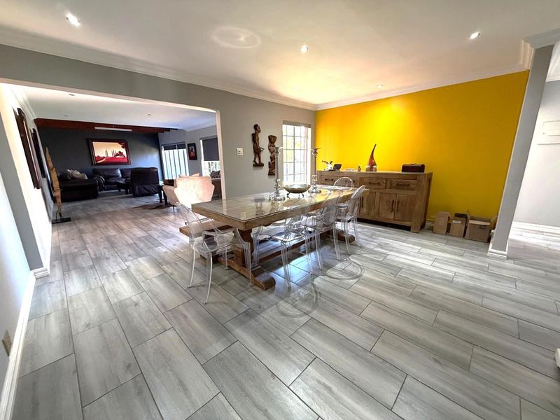 Spacious open-plan dining area featuring modern wood-look tile flooring, recessed lighting, and a vibrant accent wall, flowing seamlessly into the adjacent living space.