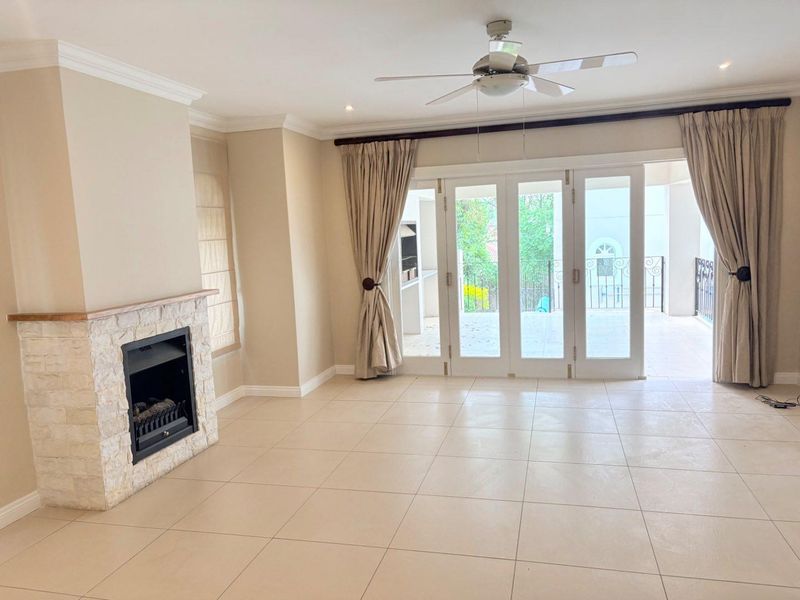 Spacious living room featuring a stone-clad fireplace, tiled flooring, and large stacking glass doors that open onto an outdoor patio area.