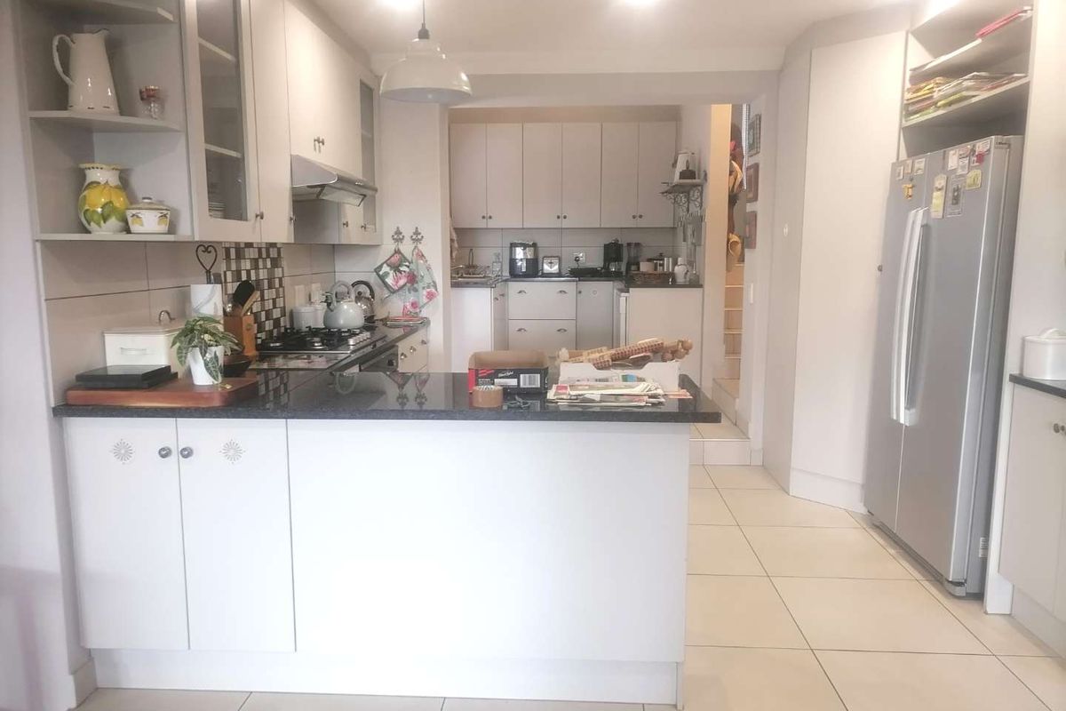 A functional kitchen featuring light-toned cabinetry, dark granite countertops, a gas hob, and tiled flooring, with an open-plan layout leading to a staircase.