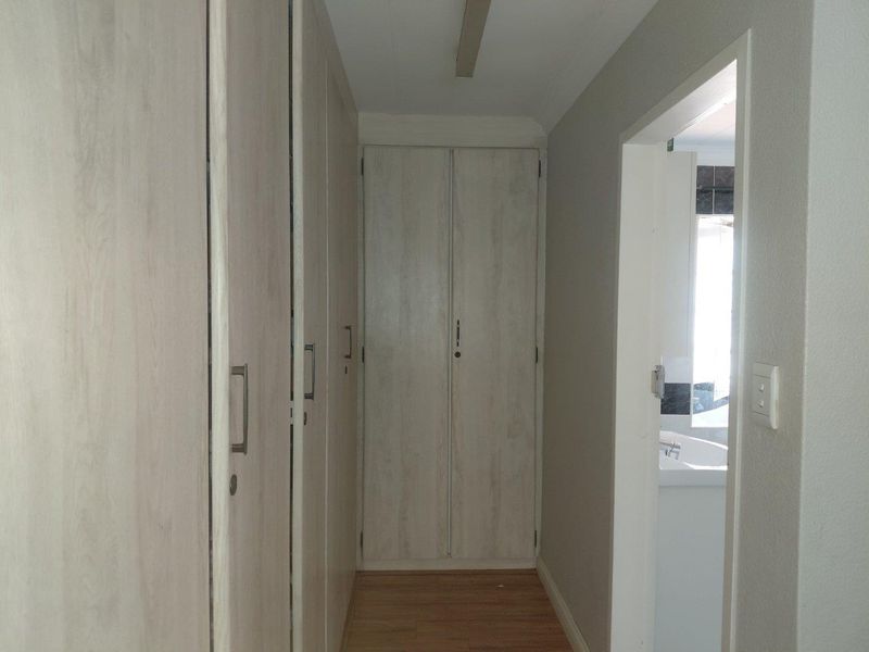 A clean hallway featuring light wood-look built-in cupboards and laminate flooring, leading towards an adjacent bathroom area.