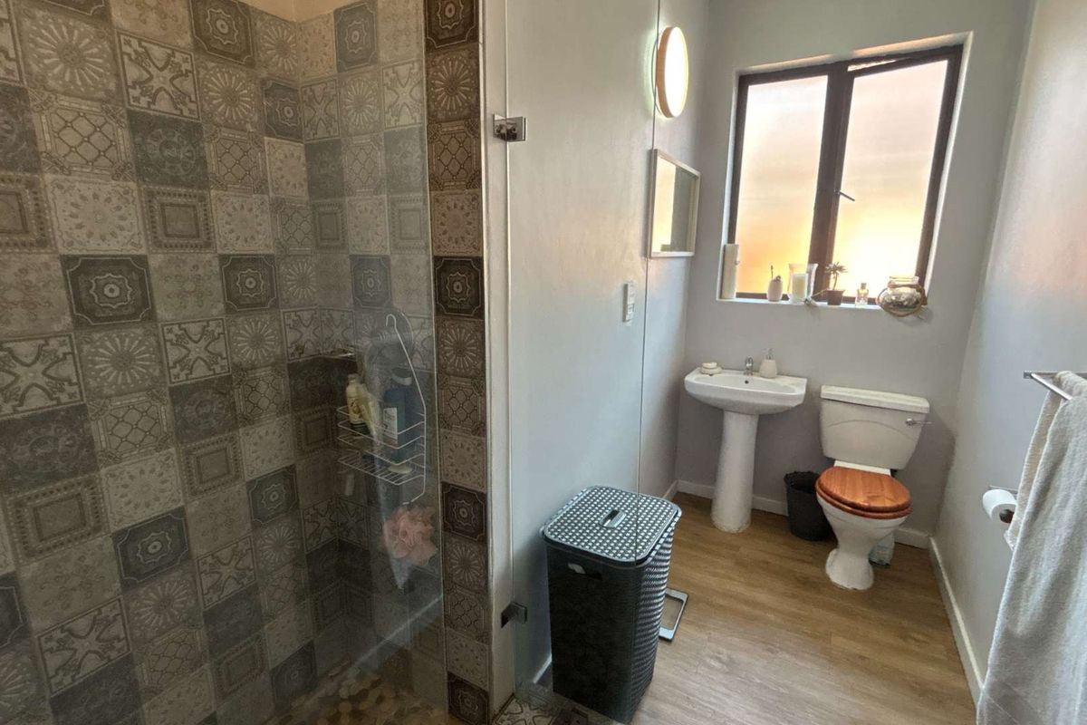A functional bathroom featuring a glass-enclosed shower with decorative patterned tiling, a pedestal basin, and a standard toilet.