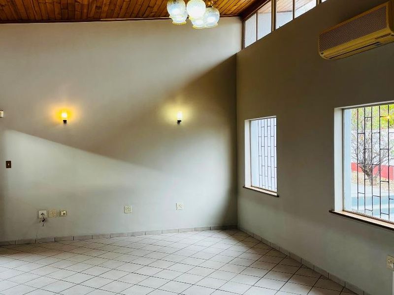 Spacious living area featuring a high timber-clad ceiling, tiled flooring, wall-mounted air conditioning, and natural light through clerestory and side windows.
