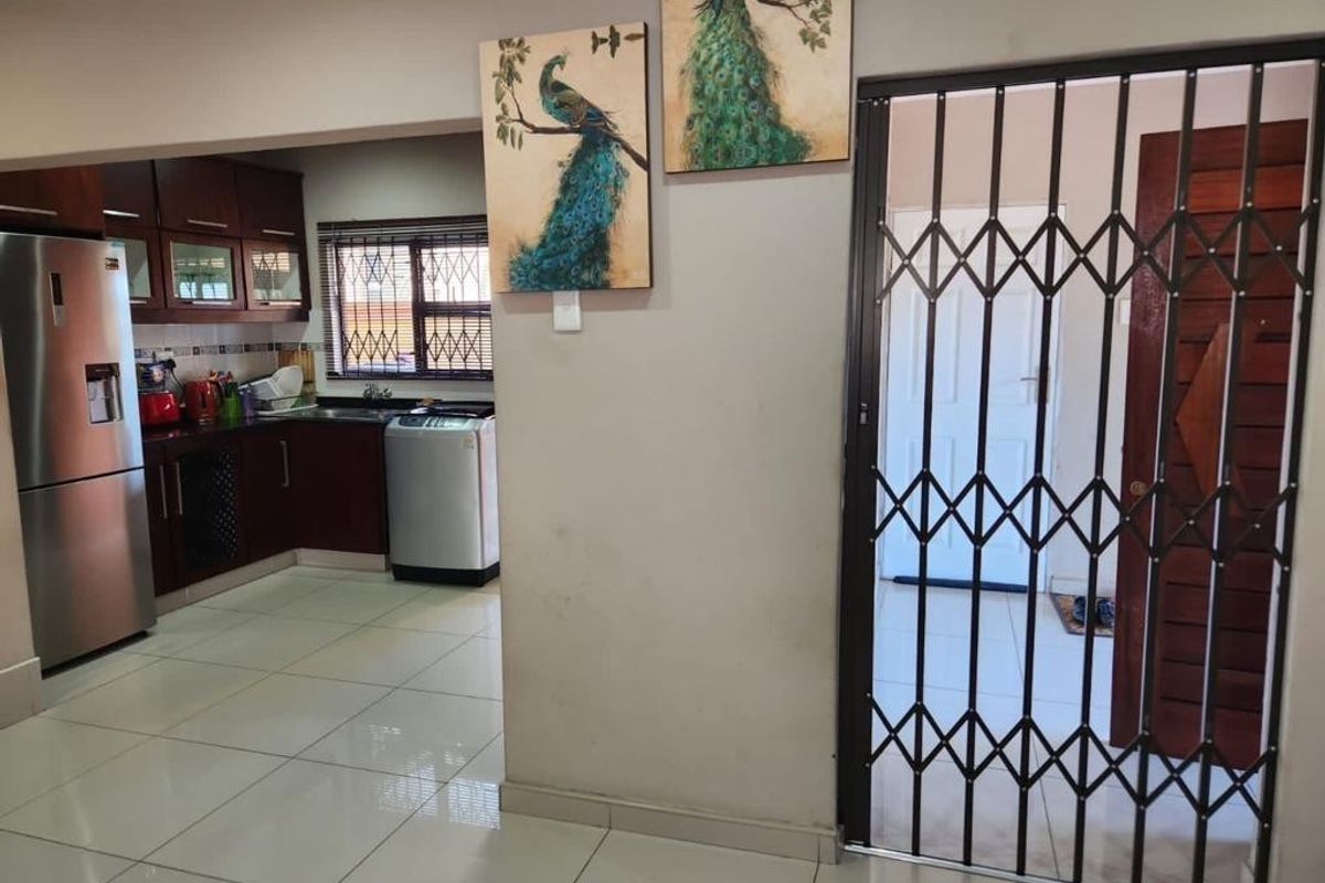A functional kitchen featuring dark wood cabinetry, tiled flooring, and a security gate leading to an adjacent area.