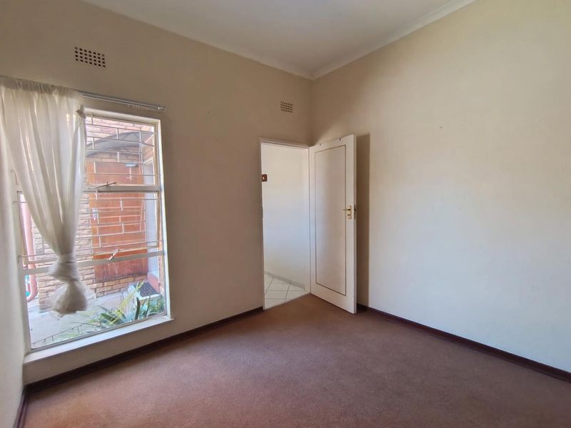 An empty bedroom featuring carpet flooring, a steel-framed window, and a standard internal door, offering a blank canvas for renovation.