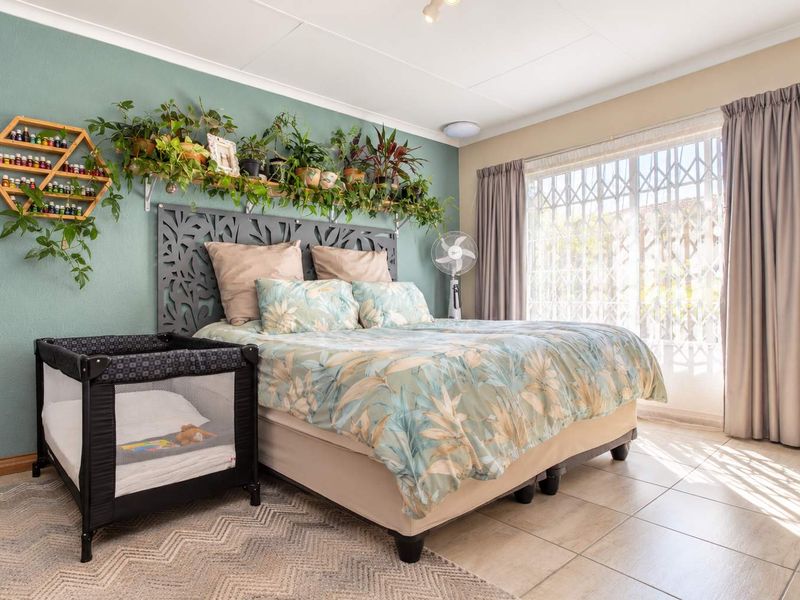 A well-lit bedroom featuring tiled flooring, a large window with security gate, and a decorative accent wall.