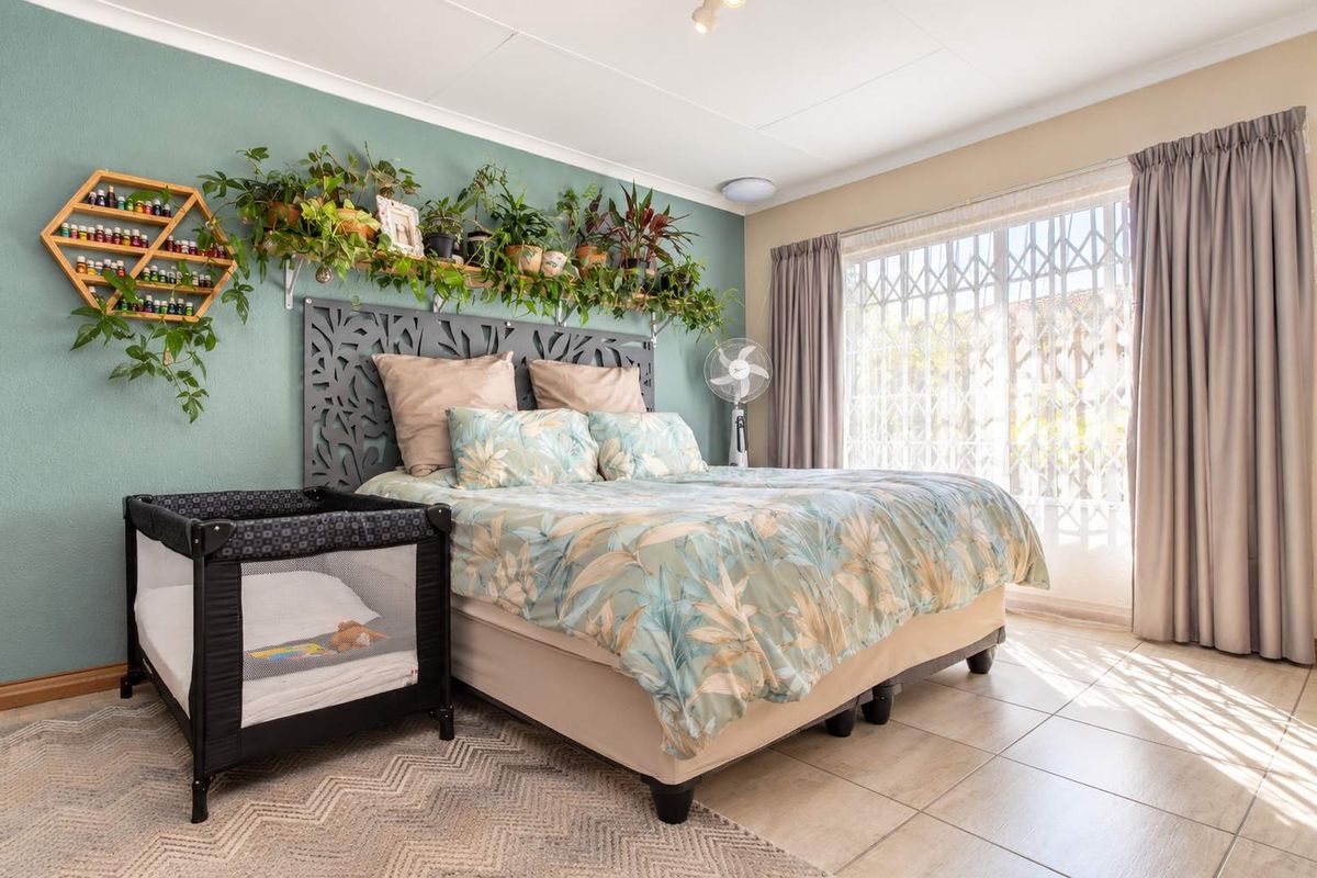 A well-lit bedroom featuring tiled flooring, a large window with security gate, and a decorative accent wall.