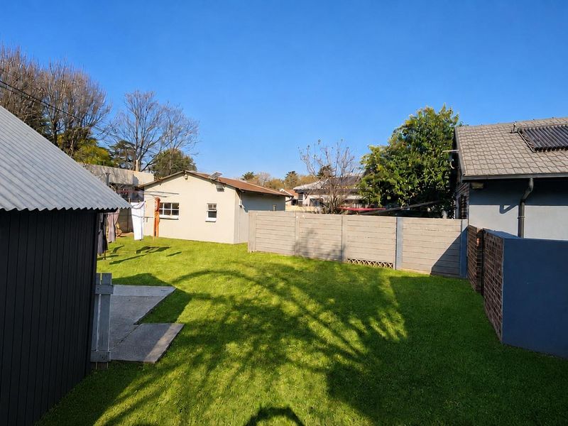 A view of the rear garden area featuring a lawn, concrete patio, and boundary walls, with a secondary structure and main house roof visible.