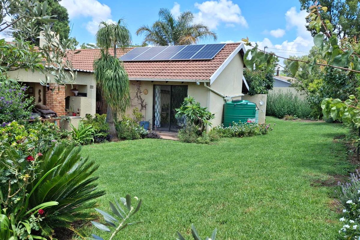 Rear view of the house featuring a tiled roof with solar panels, a water storage tank, and a covered patio area overlooking the garden.