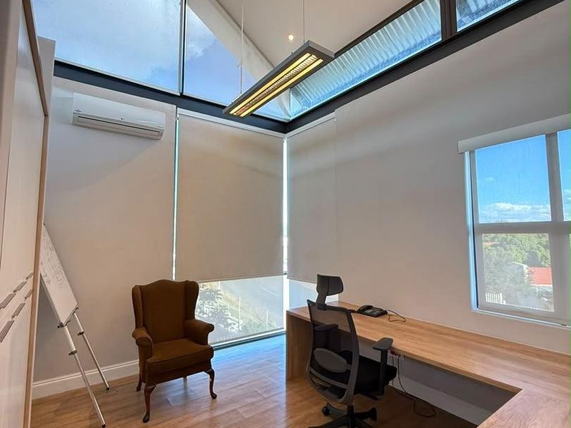 Modern office space featuring a large built-in desk, clerestory windows for natural light, split-system air conditioning, and wood-look laminate flooring.