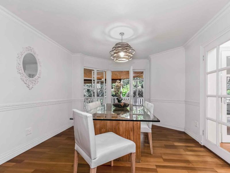 Bright dining room featuring hardwood flooring, elegant wainscoting, crown molding, and French doors leading to an outdoor area.
