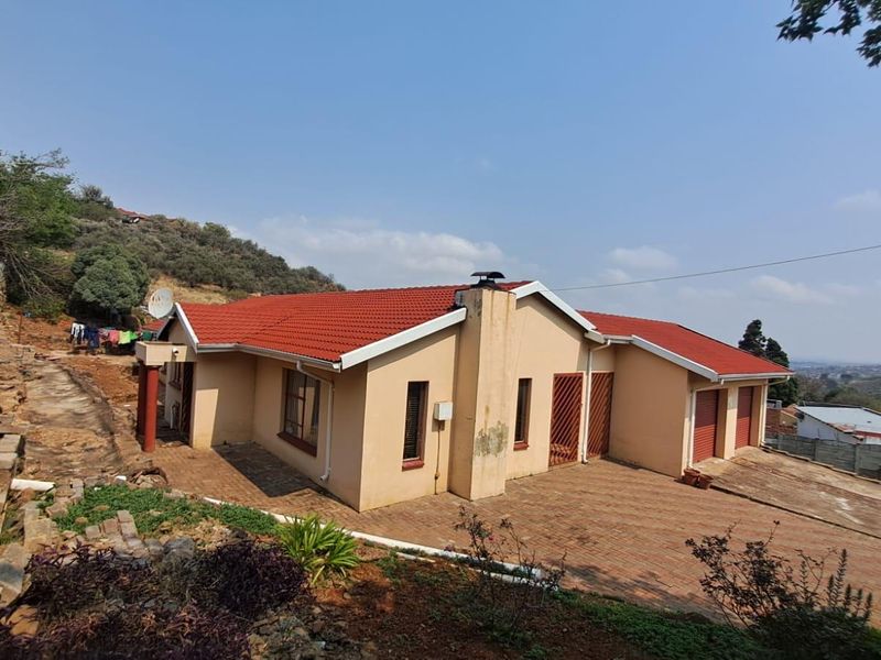 A single-story residential house featuring a red tiled roof, paved driveway, and double garage, situated on a sloped lot with hillside views.