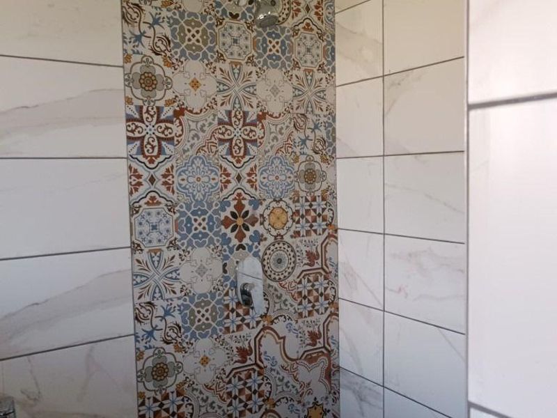 A modern bathroom shower area featuring decorative patterned accent tiles, white marble-look wall tiles, and a wall-mounted basin.