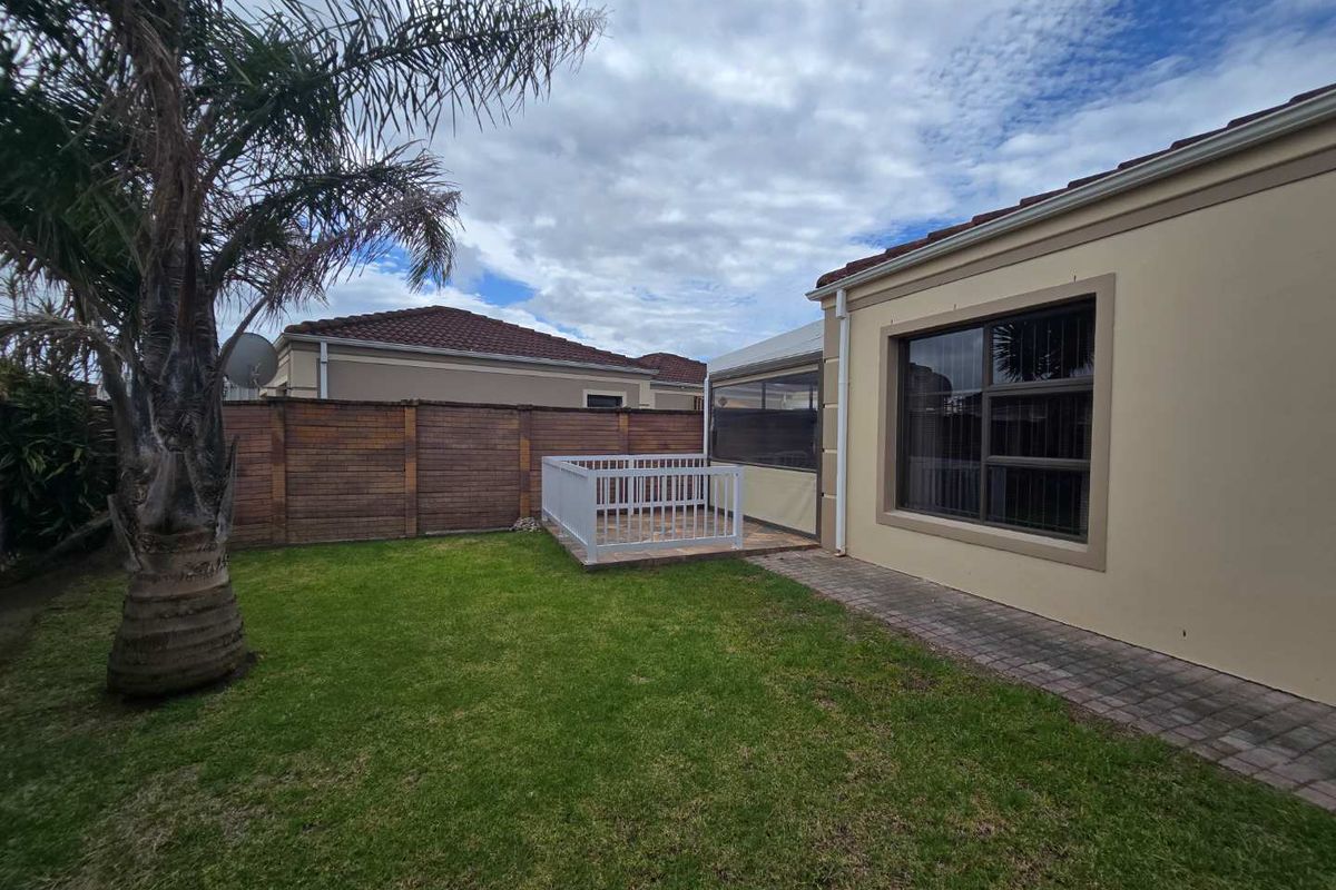 A private rear garden featuring a paved walkway, a small raised deck with white railing, and a covered patio area attached to the townhouse.