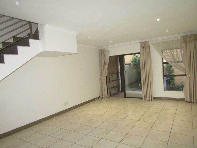 Spacious open-plan living area featuring tiled flooring, recessed lighting, and a staircase, with direct access to an outdoor patio area through sliding glass doors.