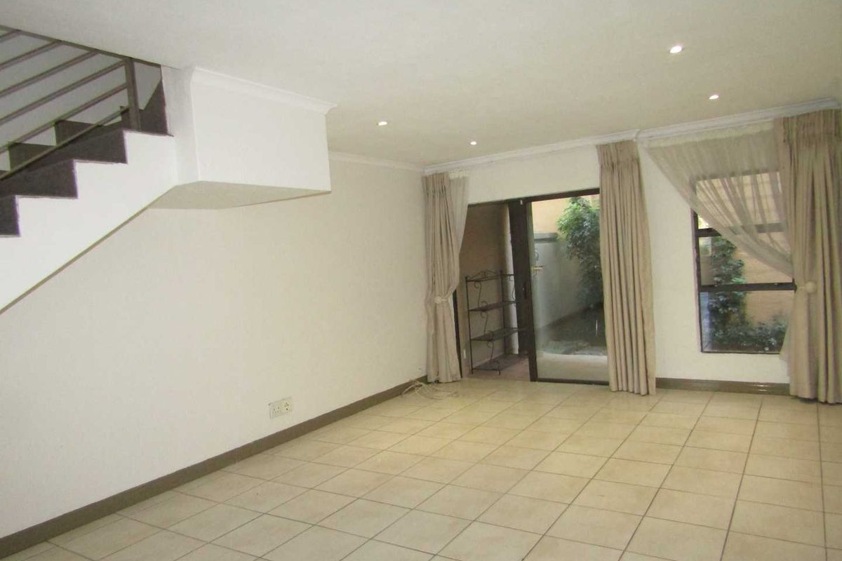 Spacious open-plan living area featuring tiled flooring, recessed lighting, and a staircase, with direct access to an outdoor patio area through sliding glass doors.