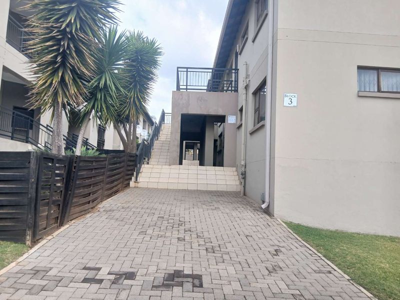 Exterior view of a townhouse complex block featuring a paved driveway, tiled staircase access, and upper-level balcony.