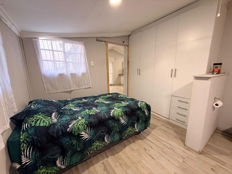 A bedroom featuring built-in wardrobes, light-toned laminate flooring, and a window with security bars, offering a functional living space.