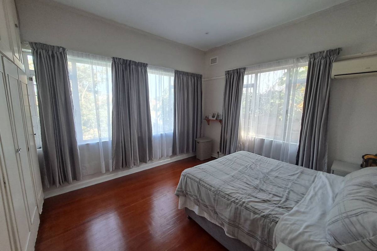 A spacious bedroom featuring polished timber flooring, built-in cabinetry, and large windows that provide ample natural light.