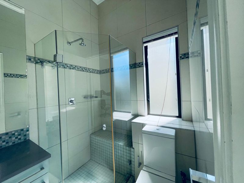 A clean, modern bathroom featuring a glass-enclosed shower, tiled walls, and a functional toilet, offering a bright and well-maintained space.