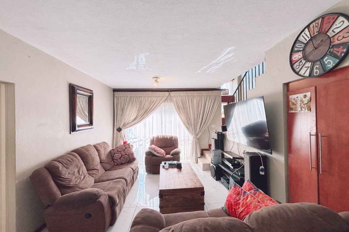 A comfortable living room featuring tiled flooring, large sliding glass doors with curtains, and an integrated staircase leading to the upper level.