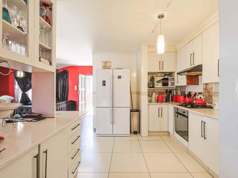 A functional kitchen featuring white built-in cabinetry, stone countertops, integrated oven and hob, and tiled flooring, leading into an adjacent living area.