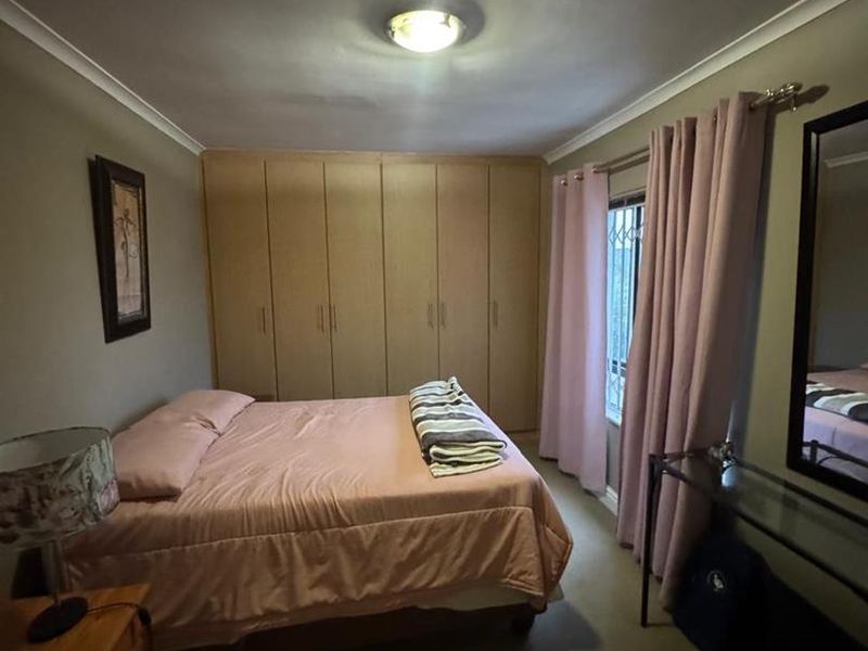 A bedroom featuring built-in cupboards, neutral wall tones, and a window fitted with a security gate.