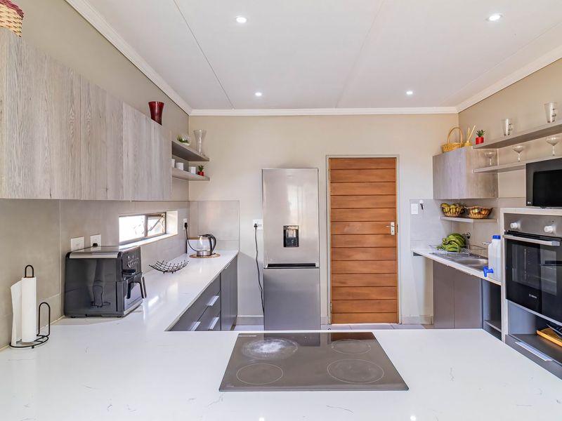 Modern kitchen featuring light wood-grain cabinetry, white quartz countertops, integrated electric hob, built-in oven, and recessed ceiling lighting.