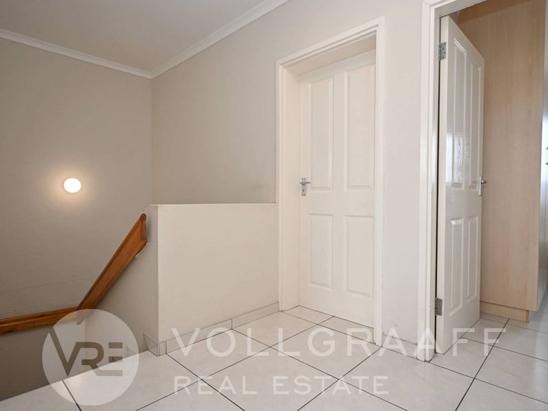 A clean and bright hallway featuring tiled flooring, a staircase handrail, and access to adjacent rooms via internal doors.