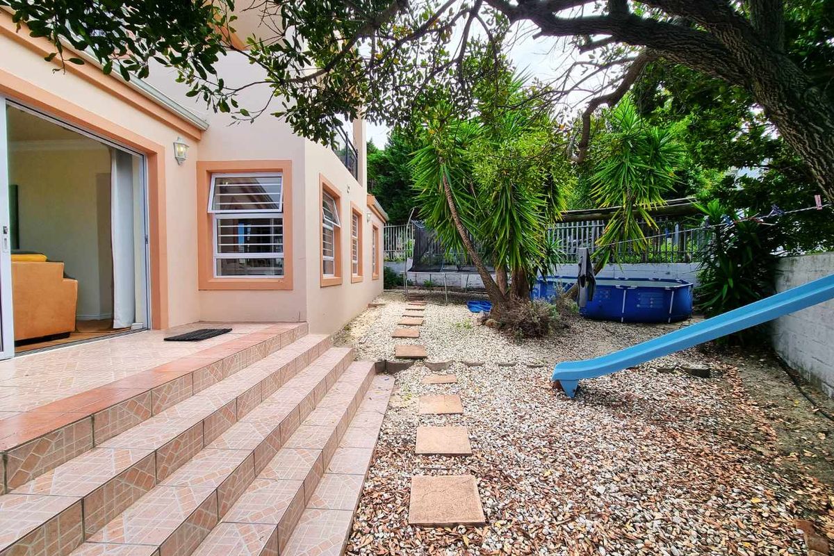Rear exterior view featuring a tiled patio area with steps leading down to a gravel garden with mature trees and boundary wall.