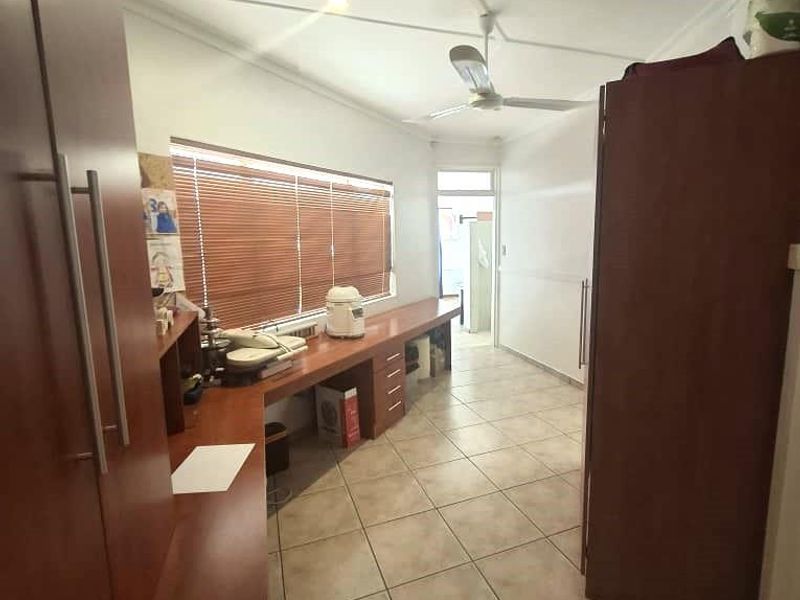 A functional home office space featuring built-in desk cabinetry, tiled flooring, and a ceiling fan, providing a practical workspace.