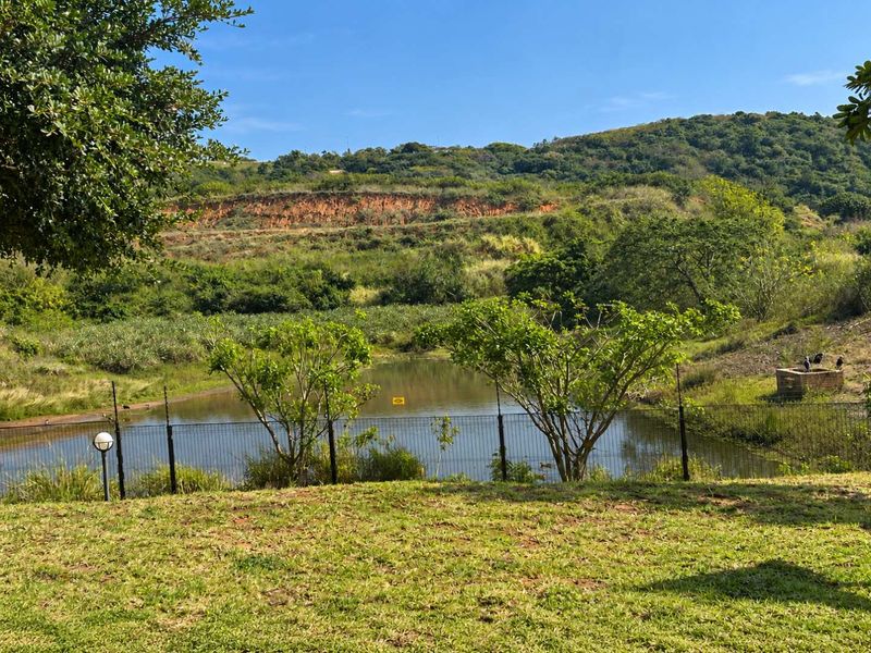 A scenic view overlooking a natural pond and landscaped hillside, featuring secure wire mesh perimeter fencing and established greenery.