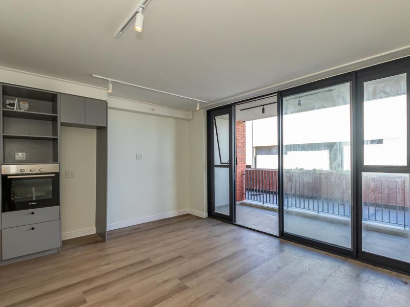 Modern open-plan living area featuring laminate flooring, built-in oven, sleek grey cabinetry, and large sliding glass doors leading to a private balcony.