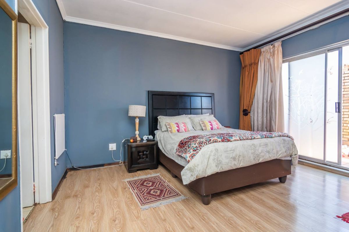 A bedroom featuring laminate flooring, blue painted walls, and a sliding glass door providing access to an outdoor area.