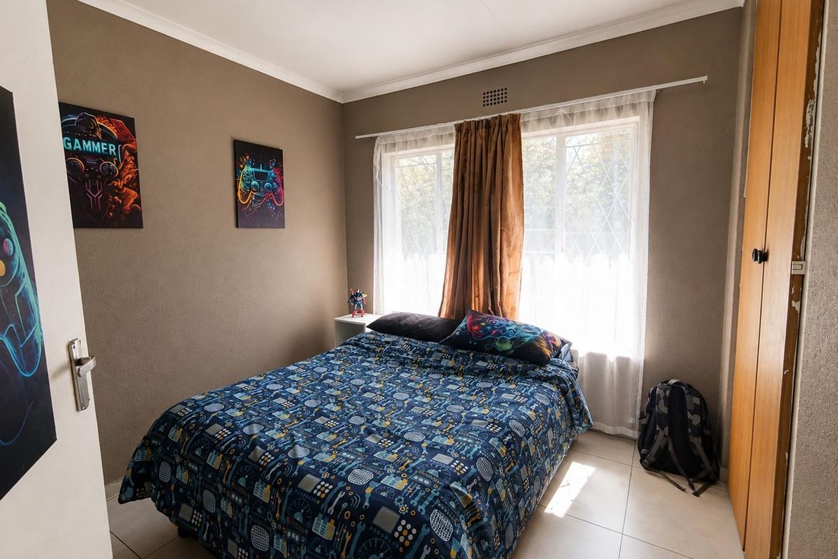 A functional bedroom featuring tiled flooring, a built-in wardrobe, and large windows with security bars, providing natural light and practical storage space.