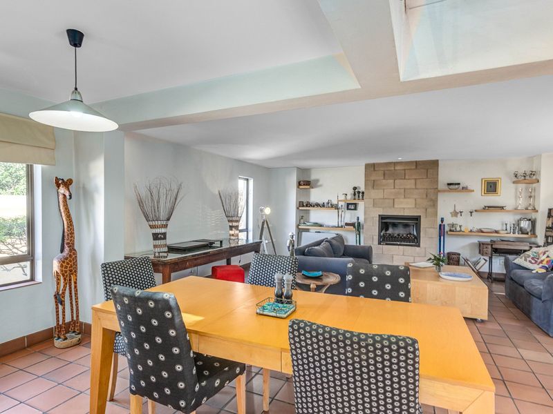 Spacious open-plan living and dining area featuring terracotta floor tiles, a prominent stone fireplace, and built-in shelving units.