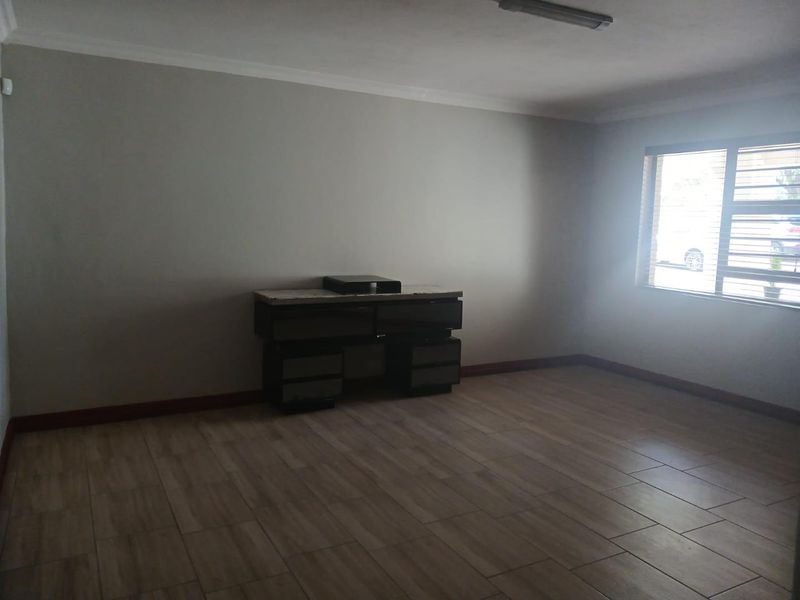 A spacious, empty living area featuring neutral tiled flooring, cove cornicing, and a window fitted with security burglar bars.
