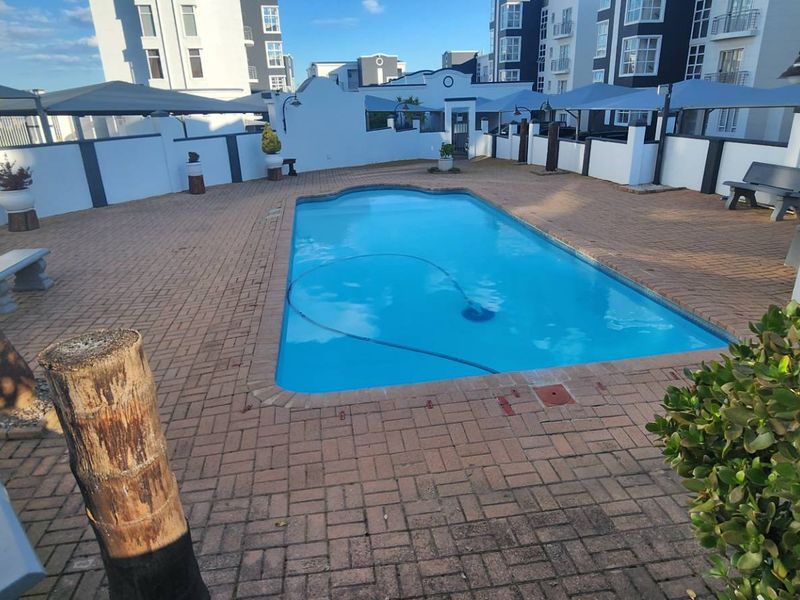 Communal swimming pool area featuring brick paving, shade sails, and perimeter walling within an apartment complex.