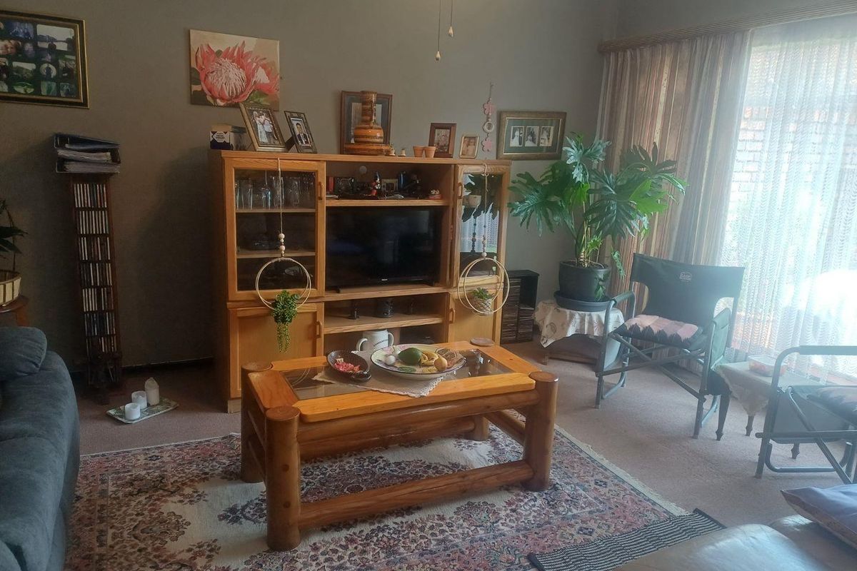 A comfortable living room featuring carpeted flooring, neutral wall tones, and large windows with curtains allowing natural light into the space.