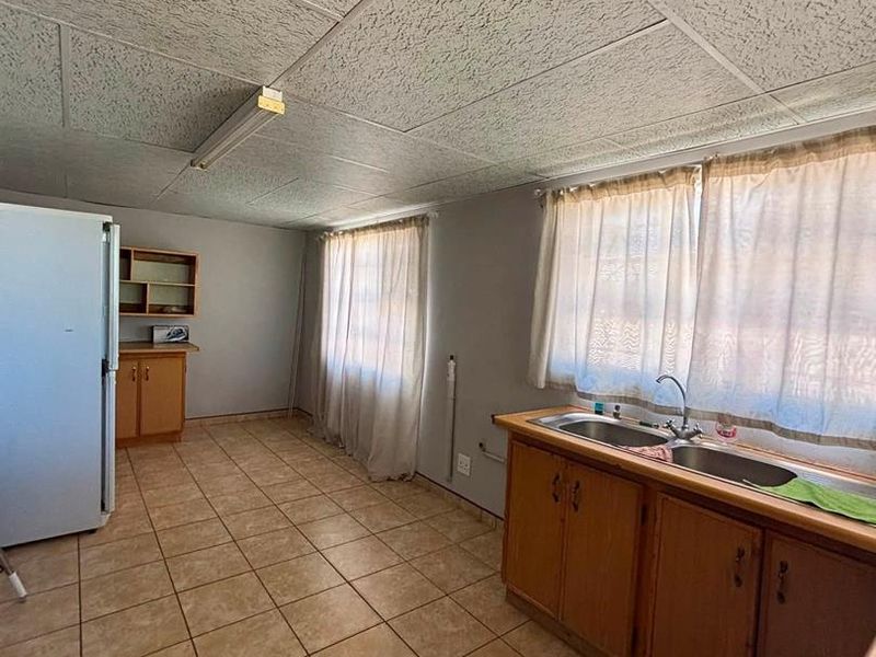 A functional kitchen featuring tiled flooring, fitted wooden cabinetry, and a double bowl sink, offering potential for modernization and aesthetic updates.